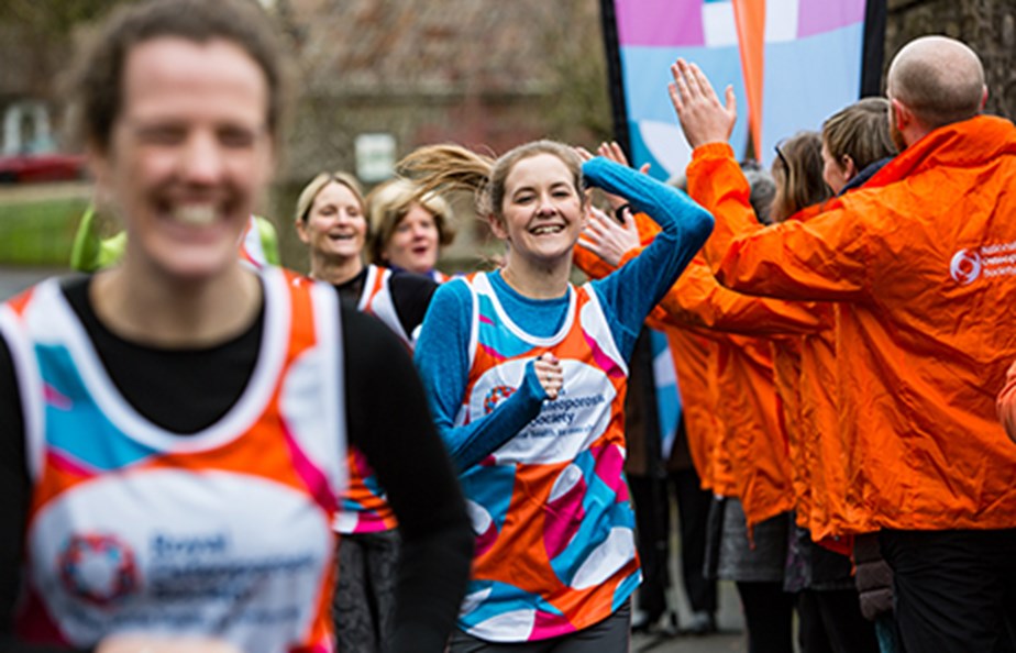 a group of runners wear ROS tops and the charity cheer team high five them as they run by 