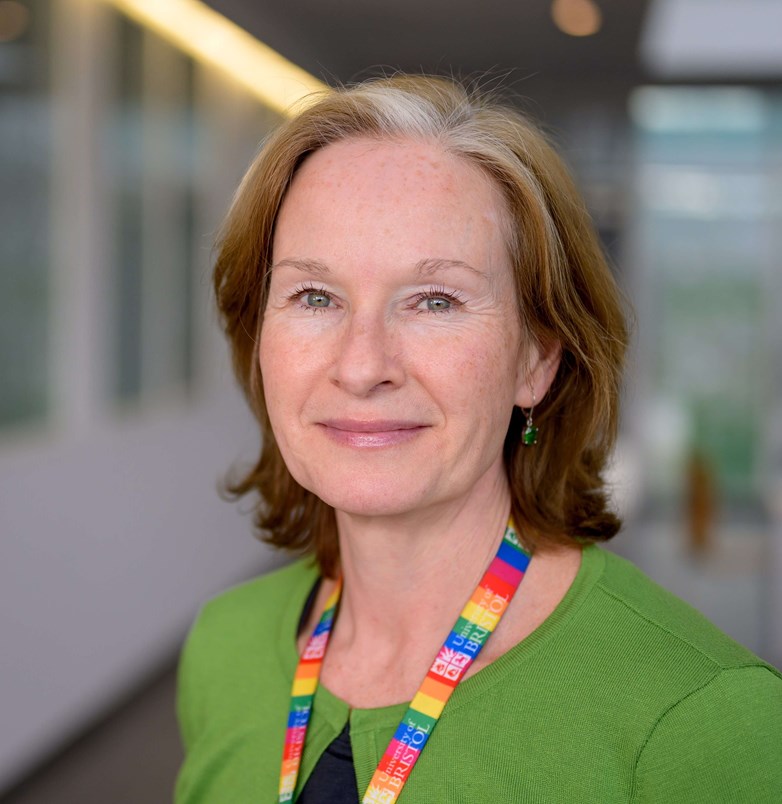 Picture of Emma Clark, a woman with ginger hair wearing a green cardigan and a rainbow lanyard around her neck