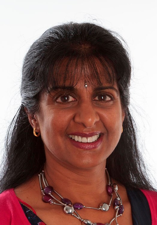 Picture of a woman smiling with long black hair, wearing a bindi and a red cardigan