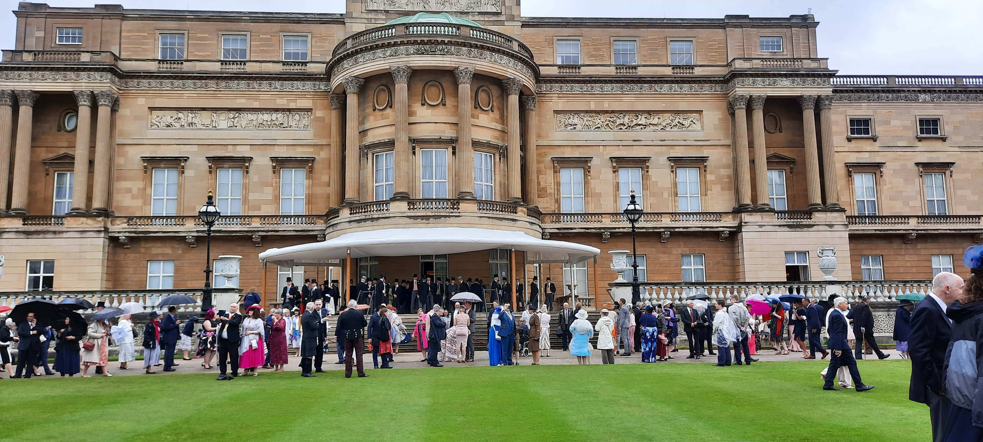 The front of Buckingham Palace with people outside on the grass