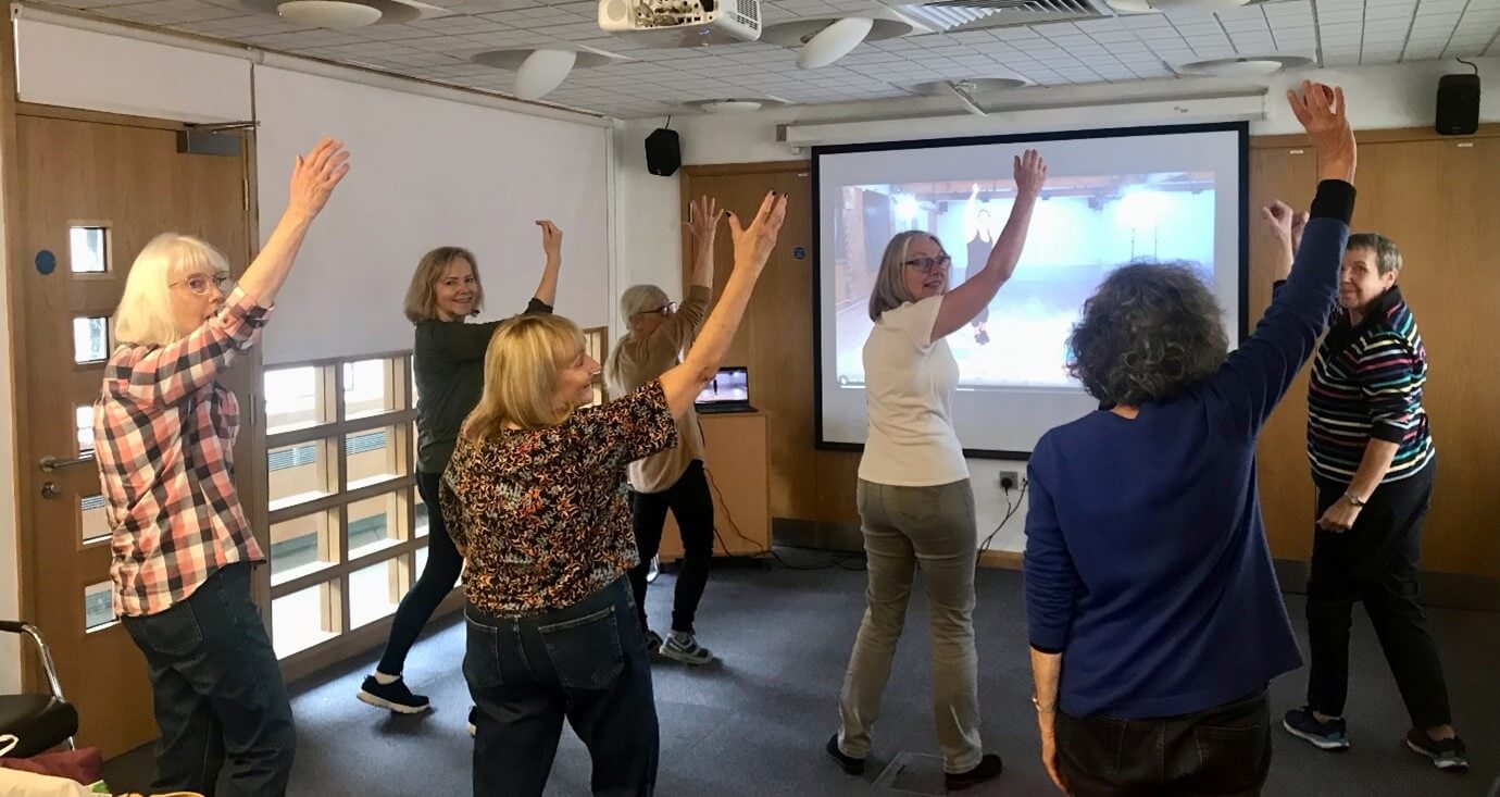 A group of volunteers from the Sheffield support group watching the video on a big screen and dancing along