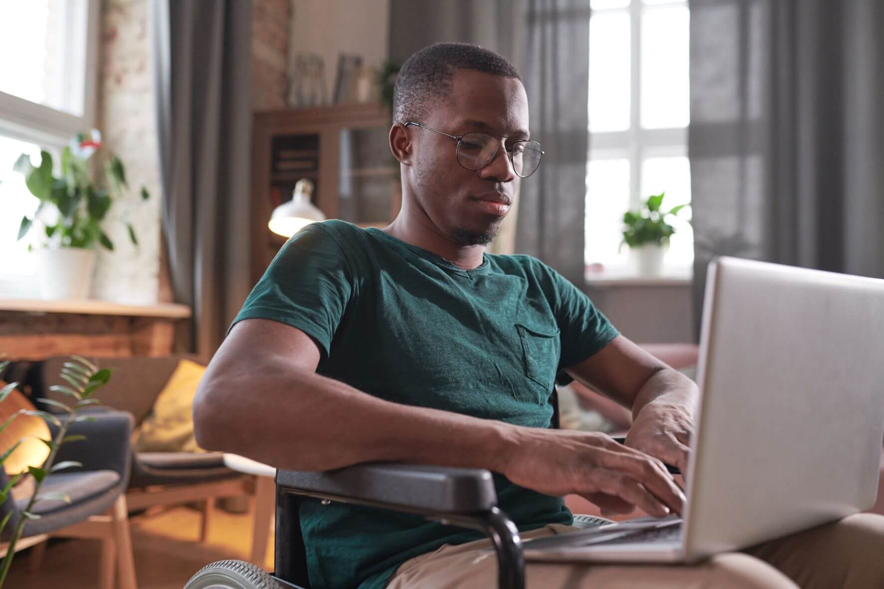 A man in a wheelchair typing on a laptop in a sitting room