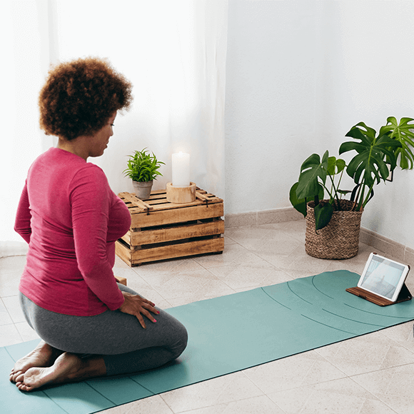 A woman knelt on a yoga mat looking at a computer tablet device