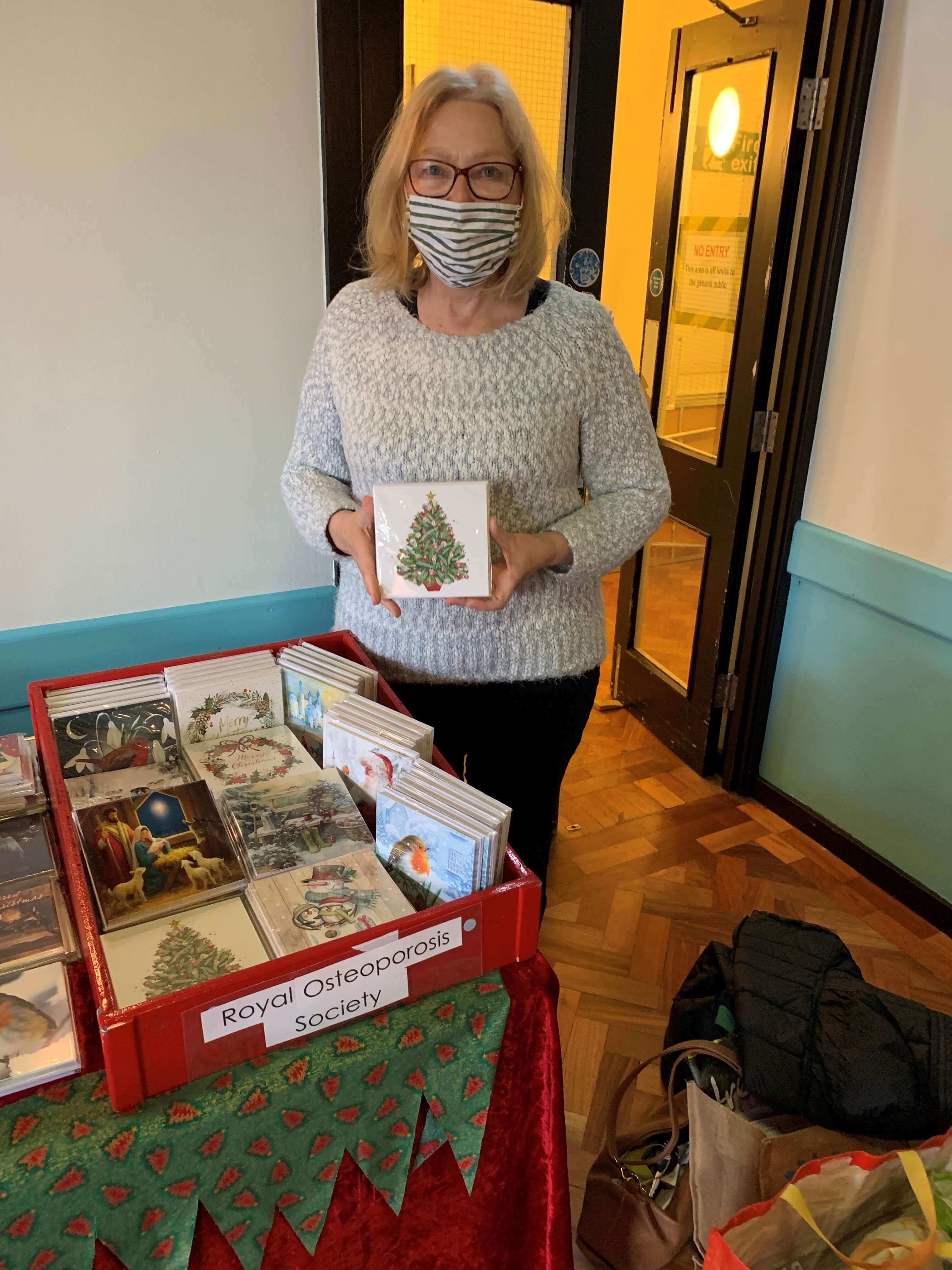 A woman wearing a face covering standing next to packs of Christmas cards on a stand