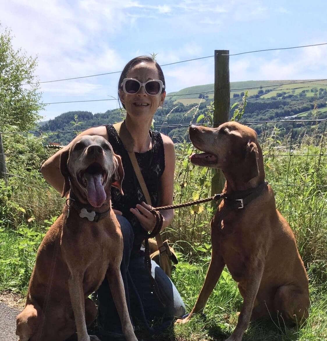 Head of Volunteering and Public Engagement, Helen, wearing sunglasses in the countryside with two dogs