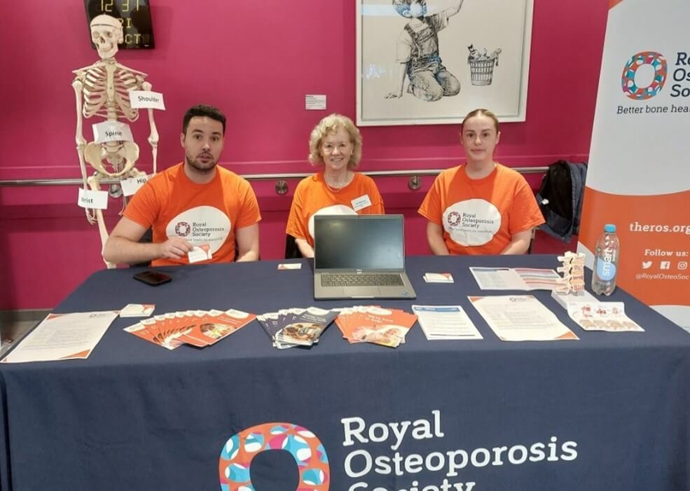 Three people in orange ROS tshirts sit behind a table covered in leaflets