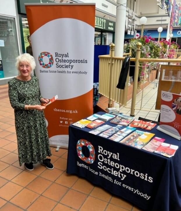 ROS volunteer stands next to a pull up banner and table covered in ROS leaflets