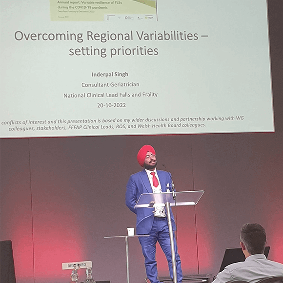 Dr Inderpal Singh standing on a stage delivering a presentation in front of a projector screen